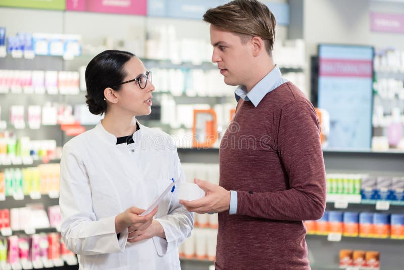 Jeune homme lisant la prescription d'une médecine importante à côté d'un pharmacien photographie stock Jeune homme lisant la prescription d'une médecine importante à côté d'un pharmacien photographie stock