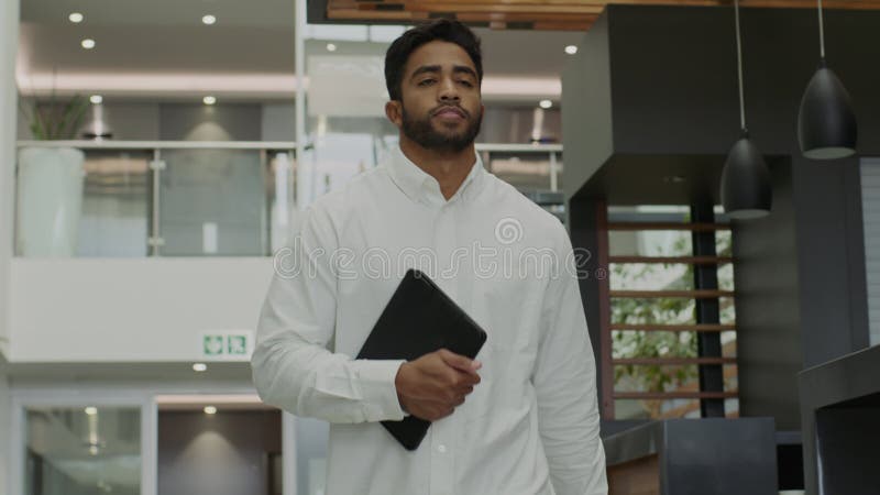 Jeune homme multiracial en chemise tenant une tablette numérique en marchant au bureau