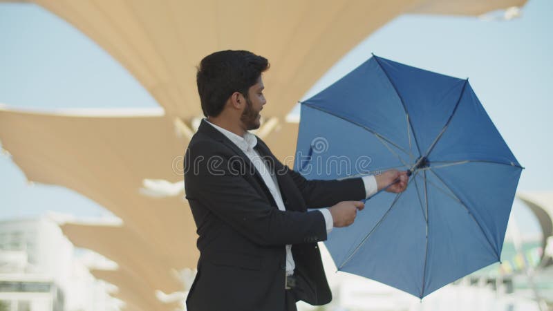 Jeune homme musulman darkhaïen teste un parapluie bleu dehors. banque de vidéos