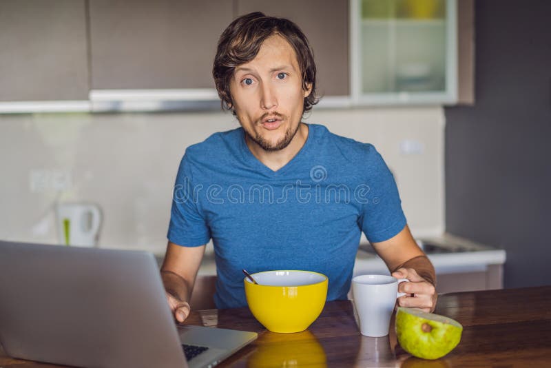 Jeune homme prenant le petit d?jeuner et ? l'aide de l'ordinateur portable sur la cuisine photographie stock libre de droits Jeune homme prenant le petit d?jeuner et ? l'aide de l'ordinateur portable sur la cuisine photographie stock libre de droits