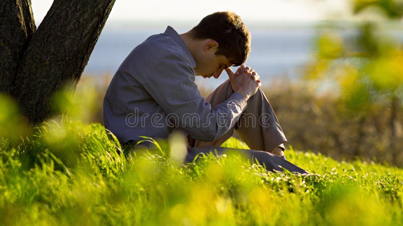 Jeune homme priant à Dieu dans la nature cintrant sa tête à ses genoux, religion de concept