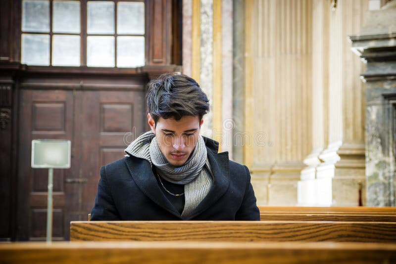 Jeune homme s'asseyant et prière d'agenouillement dans l'église image stock Jeune homme s'asseyant et prière d'agenouillement dans l'église image stock