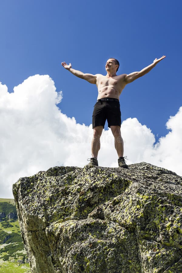 Jeune homme se tenant sur une falaise avec des bras augmentés photographie stock libre de droits Jeune homme se tenant sur une falaise avec des bras augmentés photographie stock libre de droits