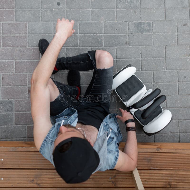 Jeune homme sportif beau s'asseyant sur une étape en bois à côté d'un hoverboard blanc moderne Vue supérieure sur le type à la mo images stock Jeune homme sportif beau s'asseyant sur une étape en bois à côté d'un hoverboard blanc moderne Vue supérieure sur le type à la mo images stock