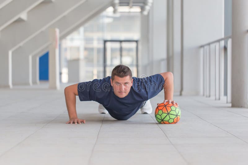 Jeune homme sportif faisant des pousées avec la boule du football image libre de droits Jeune homme sportif faisant des pousées avec la boule du football image libre de droits