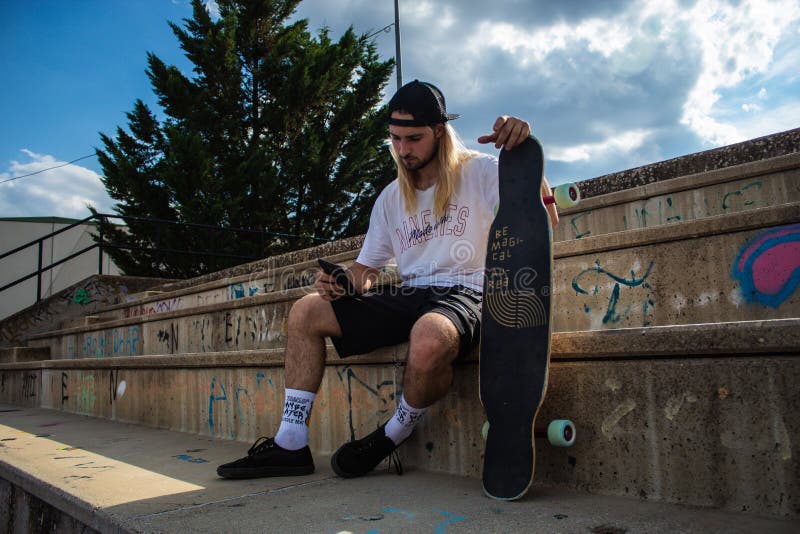 Jeune homme sportif lire un message en ligne sur téléphone sur skateboard. branché hipster assis sur patinage avec téléphone porta