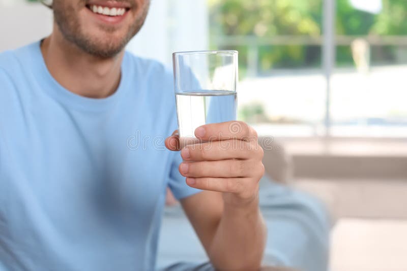 Jeune homme tenant le verre d'eau propre à l'intérieur photographie stock libre de droits Jeune homme tenant le verre d'eau propre à l'intérieur photographie stock libre de droits