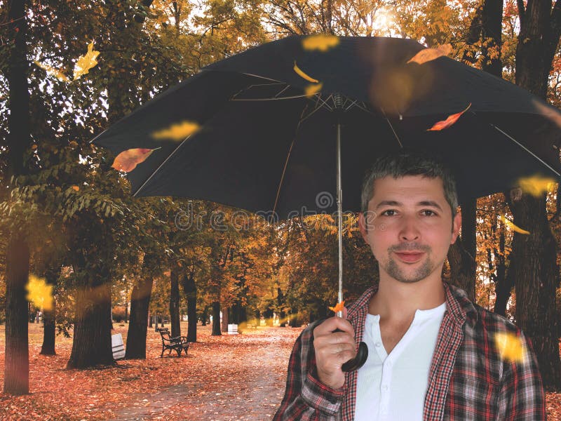 Jeune homme tenant un parapluie à feuilles d'automne tombant autour images stock Jeune homme tenant un parapluie à feuilles d'automne tombant autour images stock