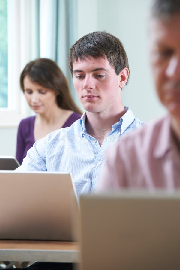 Jeune homme travaillant sur l'ordinateur portable dans la classe d'éducation des adultes photos stock