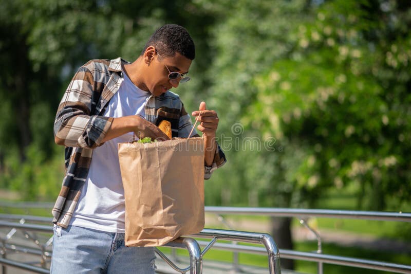 Jeune homme à la peau foncée avec un sac en papier de nourriture photos stock