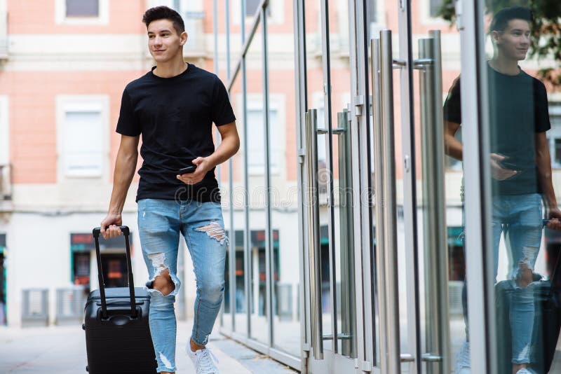 Jeune homme élégant avec le T-shirt noir et des jeans déchirés portant un bagage