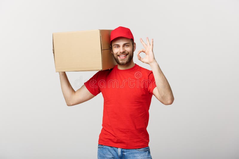 Jeune livreur gai dans le chapeau rouge se tenant avec la boîte de service des colis postaux d'isolement au-dessus du fond blanc image stock Jeune livreur gai dans le chapeau rouge se tenant avec la boîte de service des colis postaux d'isolement au-dessus du fond blanc image stock