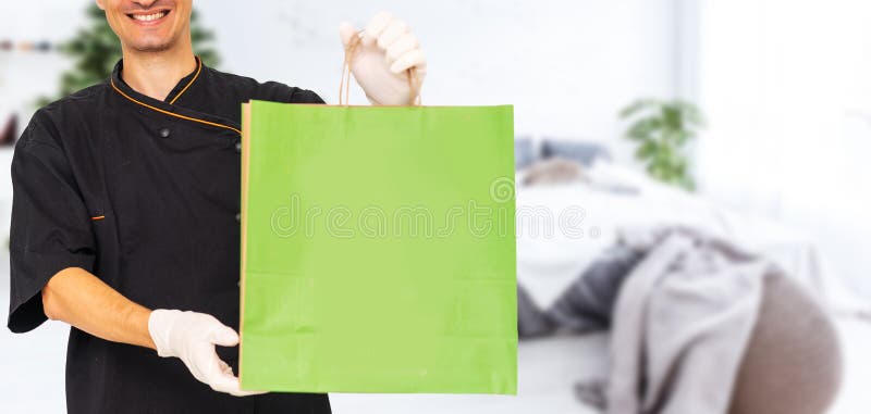Jeune livreur joli tenant sac en papier avec nourriture à emporter heureux avec grand sourire. photos stock