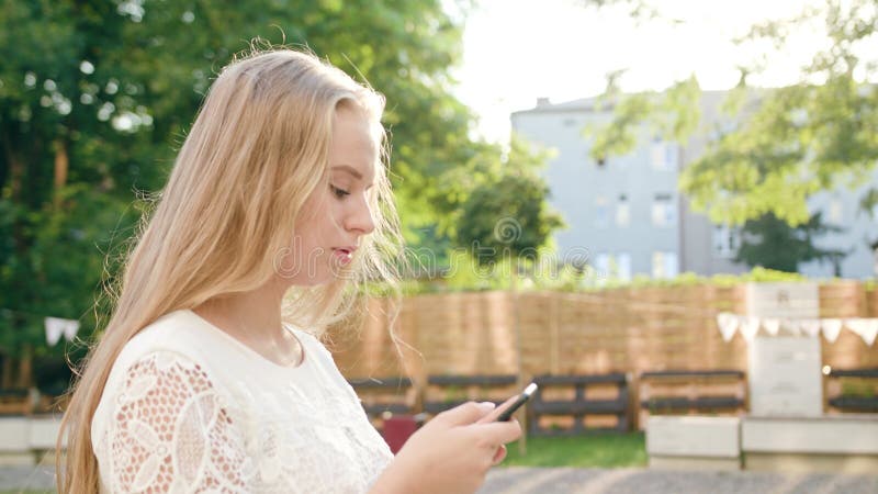 Jeune Madame blonde Walking et utilisant un téléphone en ville photographie stock Jeune Madame blonde Walking et utilisant un téléphone en ville photographie stock