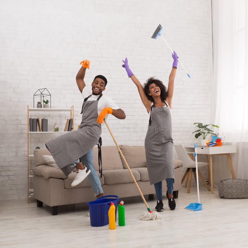 Jeune maison de nettoyage de couples, ayant l'amusement avec le balai et le balai image stock Jeune maison de nettoyage de couples, ayant l'amusement avec le balai et le balai image stock