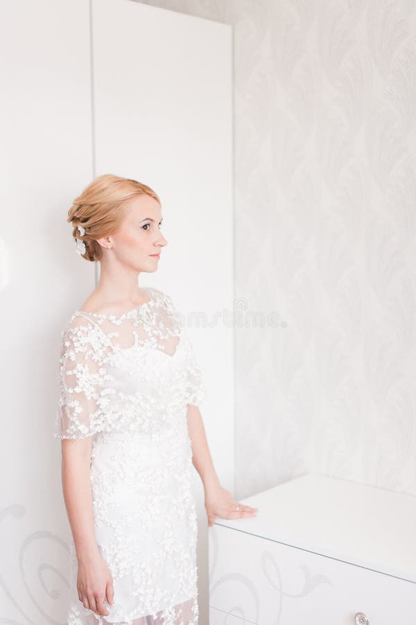 Jeune mariée magnifique avec le maquillage et la coiffure de bouquet de mariage dans la robe nuptiale à la maison attendant le ma photo libre de droits Jeune mariée magnifique avec le maquillage et la coiffure de bouquet de mariage dans la robe nuptiale à la maison attendant le ma photo libre de droits