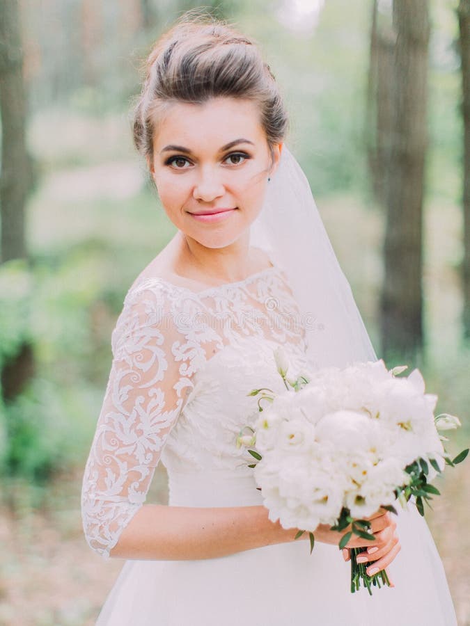 Jeune mariée merveilleuse avec le bouquet de mariage passant le temps dans le portrait en buste de forêt photographie stock