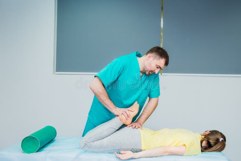Jeune massage de réception femelle du chiroprakteur du thérapeute A étirant sa jambe patiente du ` s dans le bureau médical Médic photo libre de droits Jeune massage de réception femelle du chiroprakteur du thérapeute A étirant sa jambe patiente du ` s dans le bureau médical Médic photo libre de droits