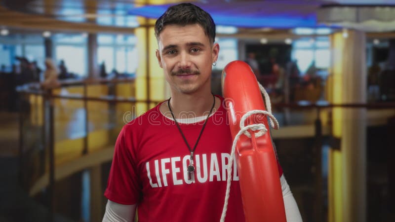 Jeune maître nageur hispanique tenant bouée avec le sourire confiant dans le cadre moderne de l'hôtel intérieur assurant la sécuri banque de vidéos