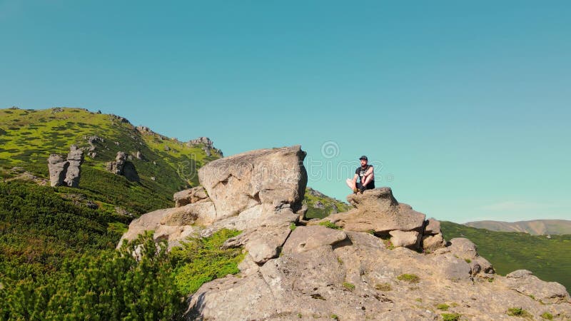 Jeune mâle assis au sommet d'une montagne vue aérienne. randonneur assis sur le bord d'une falaise en regardant clips vidéos