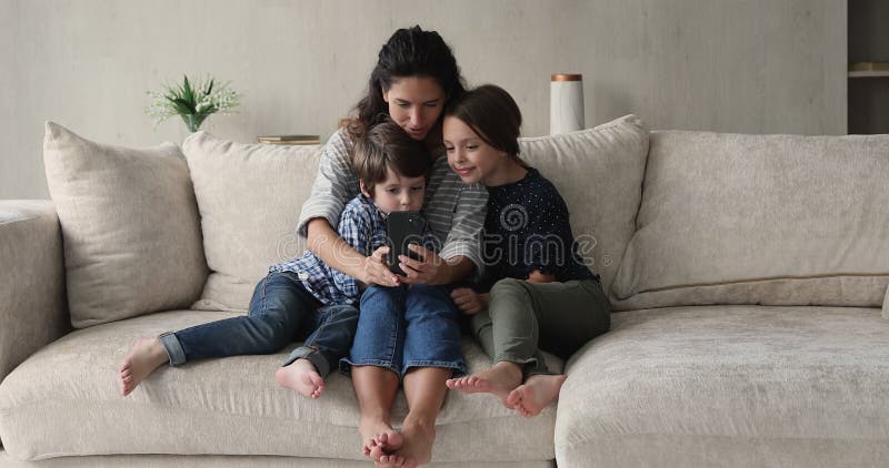 Jeune mère hispanique attentionnée utilisant un téléphone portable avec petits enfants. clips vidéos