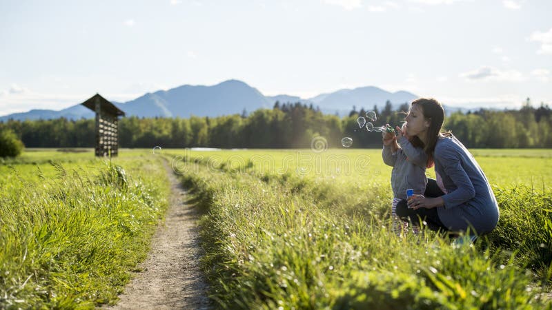 Jeune mère se mettant à genoux vers le bas à son pouvoir adiathermique de soufflement de bulles de savon d'enfant photographie stock libre de droits