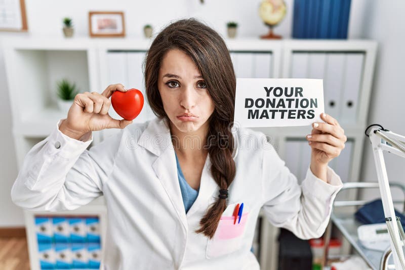 Young doctor woman holding your donation matters banner at the clinic depressed and worry for distress, crying angry and afraid. sad expression. Young doctor woman holding your donation matters banner at the clinic depressed and worry for distress, crying angry and afraid. sad expression