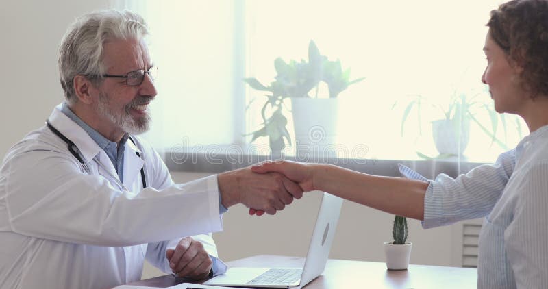 Jeune patient sourire féminin serrer la main du médecin mature heureux. banque de vidéos