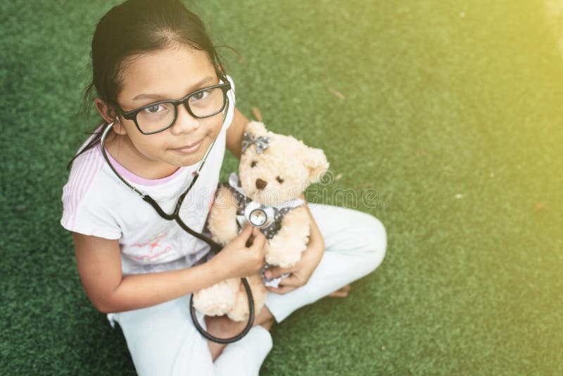 Jeune petit jouer asiatique de fille feignent pour être un docteur eaxamine de jeune fille son ours de nounours avec le stéthosco photographie stock libre de droits Jeune petit jouer asiatique de fille feignent pour être un docteur eaxamine de jeune fille son ours de nounours avec le stéthosco photographie stock libre de droits
