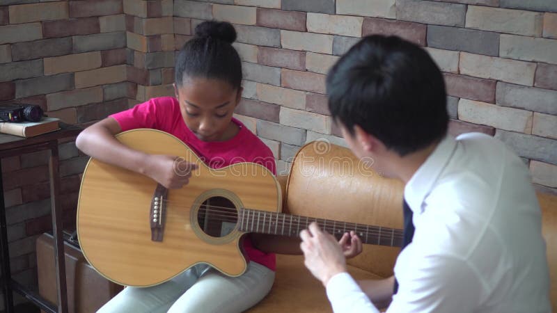 Jeune professeur masculin asiatique donnant une le?on de guitare et enseignant comment jouer la guitare ? la fille d'Afro-am?rica