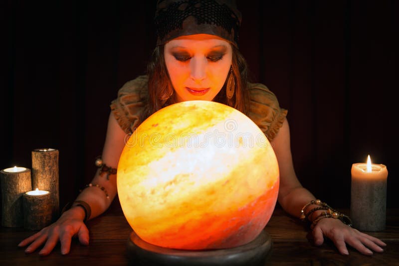 Young beautiful Psychic is telling the future, crystal ball and candles in front of black background. Young beautiful Psychic is telling the future, crystal ball and candles in front of black background