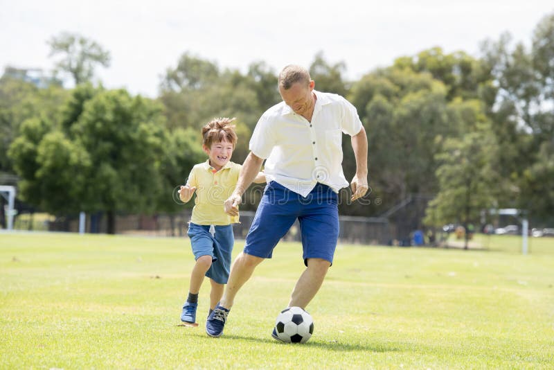 Jeune père heureux et excité peu 7 ou 8 années de fils jouant ensemble le football du football sur le jardin de parc de ville fon photographie stock libre de droits Jeune père heureux et excité peu 7 ou 8 années de fils jouant ensemble le football du football sur le jardin de parc de ville fon photographie stock libre de droits