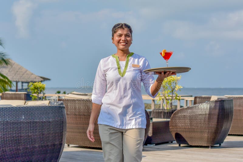 Jeune serveuse marchant avec le cocktail sur le plateau à la barre tropicale d'île image libre de droits Jeune serveuse marchant avec le cocktail sur le plateau à la barre tropicale d'île image libre de droits