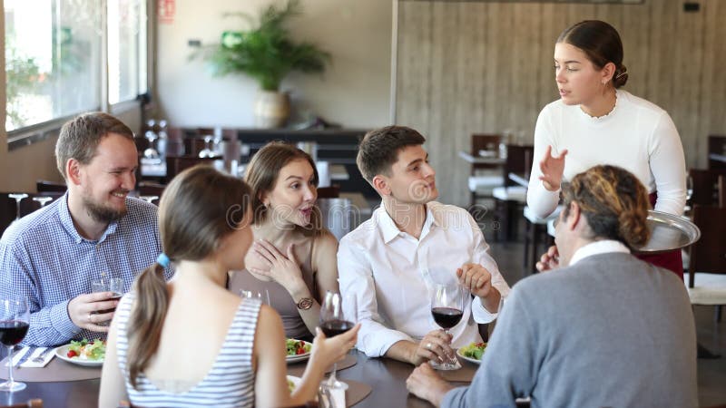 Jeune serveuse sur ordre d'un groupe d'amis à table dans le restaurant banque de vidéos