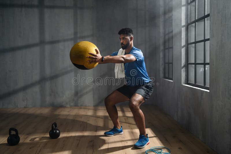 Jeune sportif afro-américain debout et levant une balle de médecine à l'intérieur d'un concept d'entraînement de travfit. images stock