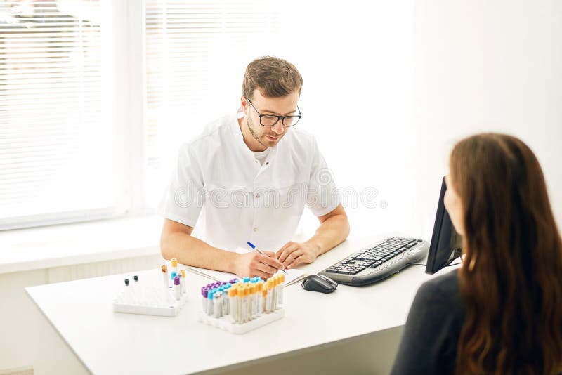 Jeune thérapeute doué écrivant une prescription à une femme malade image stock Jeune thérapeute doué écrivant une prescription à une femme malade image stock