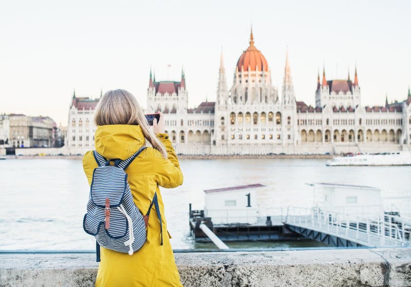 Jeune touriste blondy de femme faisant des photos du bâtiment historique du Parlement avec son téléphone à Budapest, Hongrie image stock Jeune touriste blondy de femme faisant des photos du bâtiment historique du Parlement avec son téléphone à Budapest, Hongrie image stock
