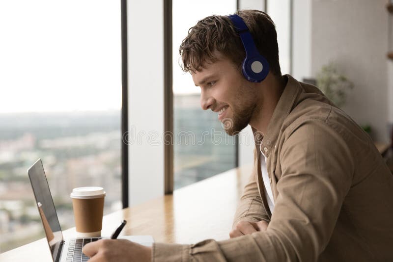 Successful man student sit by laptop take part in virtual training glad of making progress in distant learning. Skilled young male translator in headphones engaged in work by video remote interpreting. Successful man student sit by laptop take part in virtual training glad of making progress in distant learning. Skilled young male translator in headphones engaged in work by video remote interpreting