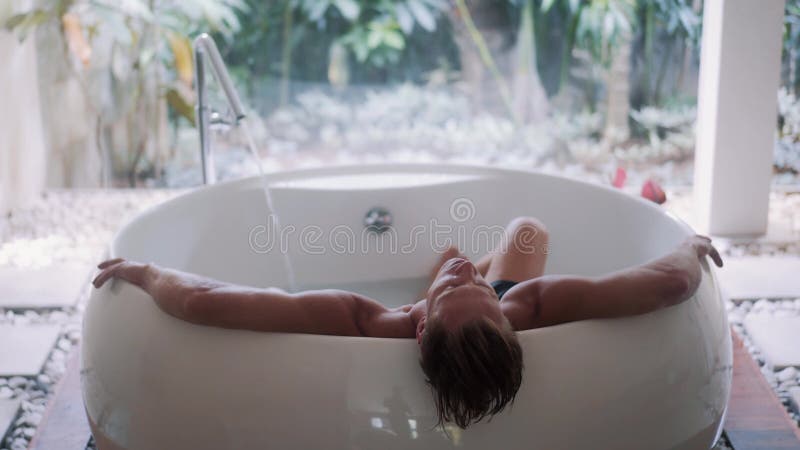 Jeune type sportif avec des repos de corps musculaire dans la grande baignoire tropicale de style à la maison