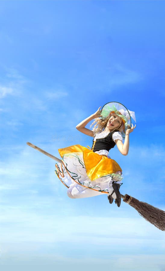 Happy young witch flying on a broom in carnival costume on a background of blue sky and white clouds. Happy young witch flying on a broom in carnival costume on a background of blue sky and white clouds