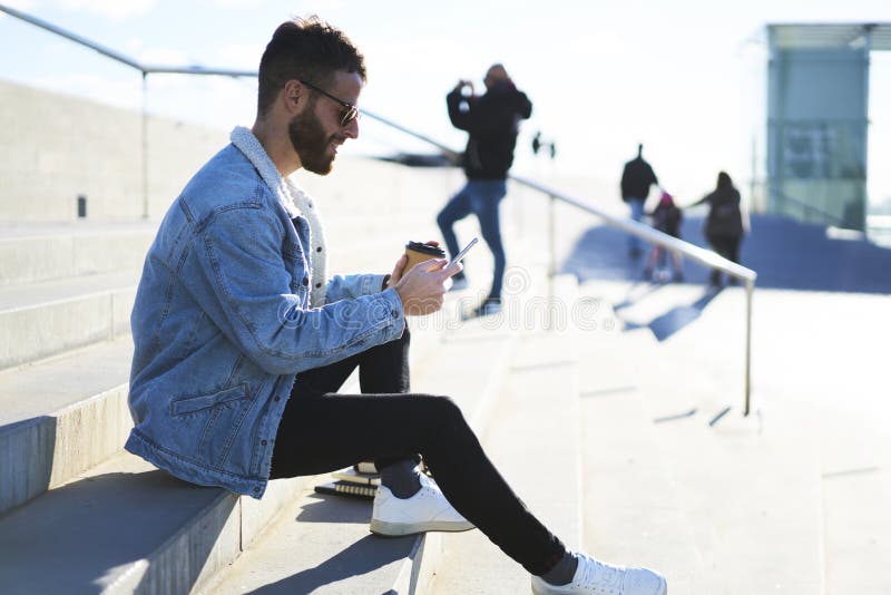 Jeune voyageur de blogger de hippie dans une veste de denim utilisant le smartphone et Internet 4G avec des amis photos libres de droits Jeune voyageur de blogger de hippie dans une veste de denim utilisant le smartphone et Internet 4G avec des amis photos libres de droits