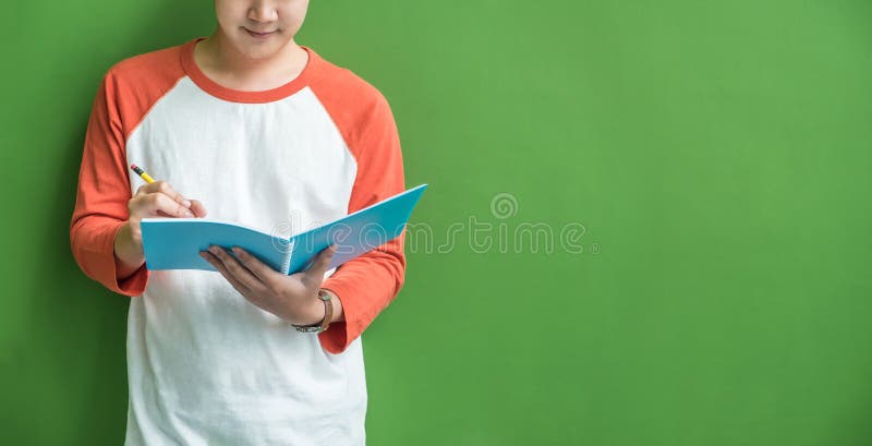 Jeune écriture de garçon d'adolescent sur le carnet bleu se penchant à wal vert photo stock Jeune écriture de garçon d'adolescent sur le carnet bleu se penchant à wal vert photo stock