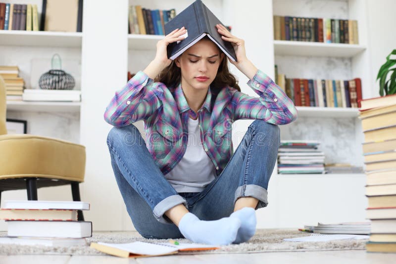 Jeune étudiante étudiant à la maison, se reposant sur le plancher contre l'intérieur domestique confortable, entouré avec la pile photographie stock Jeune étudiante étudiant à la maison, se reposant sur le plancher contre l'intérieur domestique confortable, entouré avec la pile photographie stock