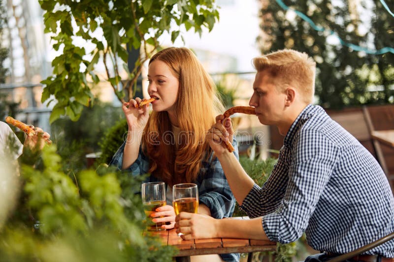 Young people, friends, couple sitting on open air restaurant, cafe pub, drinking beer, talking, having fun together. Concept of oktoberfest, traditional taste, friendship, leisure time, enjoyment. Young people, friends, couple sitting on open air restaurant, cafe pub, drinking beer, talking, having fun together. Concept of oktoberfest, traditional taste, friendship, leisure time, enjoyment