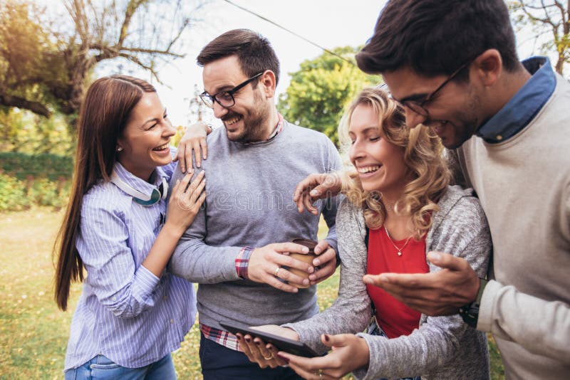 Jeunes amis de sourire heureux marchant dehors en parc tenant le comprim? num?rique photo stock Jeunes amis de sourire heureux marchant dehors en parc tenant le comprim? num?rique photo stock