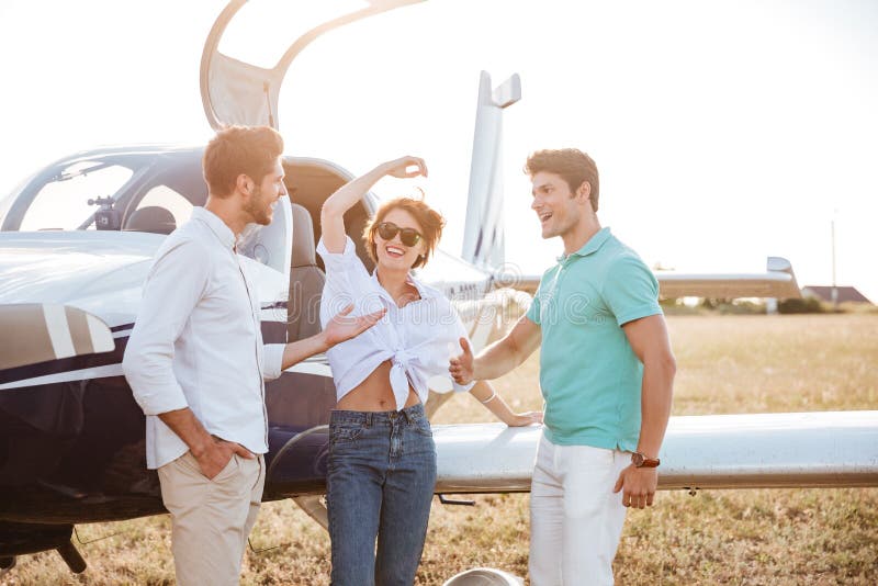 Jeunes amis gais se tenant et parlant sur la piste près de l'avion photo libre de droits Jeunes amis gais se tenant et parlant sur la piste près de l'avion photo libre de droits