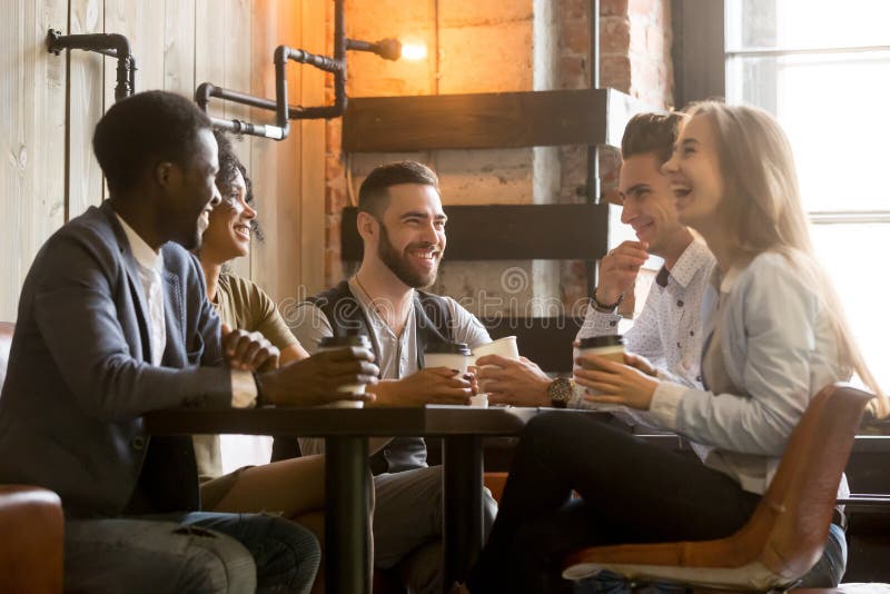 Multiracial friends having fun and laughing drinking coffee in coffeehouse, diverse young people talking joking sitting together at cafe table, multi ethnic millennials spending time in coffee shop. Multiracial friends having fun and laughing drinking coffee in coffeehouse, diverse young people talking joking sitting together at cafe table, multi ethnic millennials spending time in coffee shop