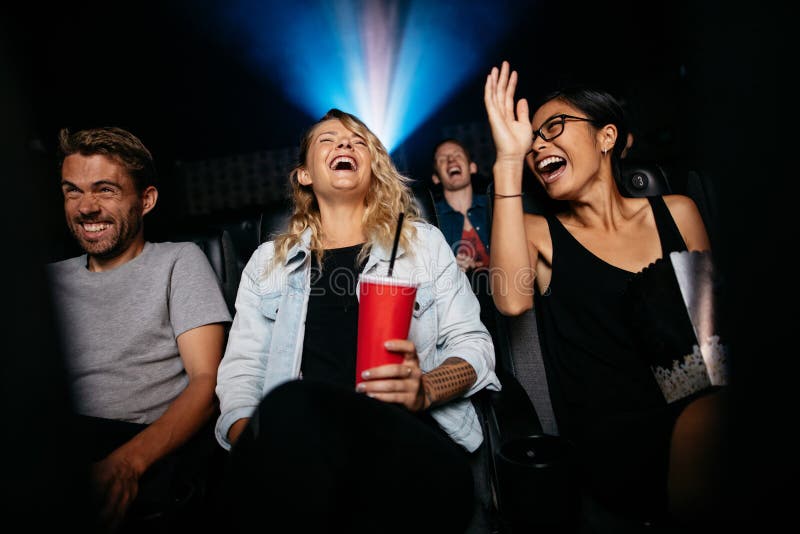 Group of people in theater with popcorn and drinks watching movie and laughing. Young women and men watching comedy movie in cinema. Group of people in theater with popcorn and drinks watching movie and laughing. Young women and men watching comedy movie in cinema.