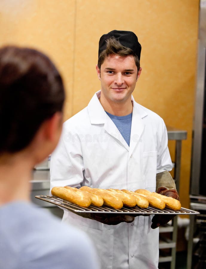 Glowing young male baker holding baguettes in the kitchen of his bakery. Glowing young male baker holding baguettes in the kitchen of his bakery