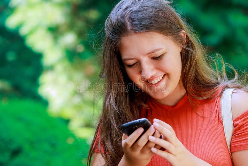 Jeunes bons messages de l'adolescence de sourire de lecture de fille dans les réseaux sociaux un téléphone portable photographie stock Jeunes bons messages de l'adolescence de sourire de lecture de fille dans les réseaux sociaux un téléphone portable photographie stock